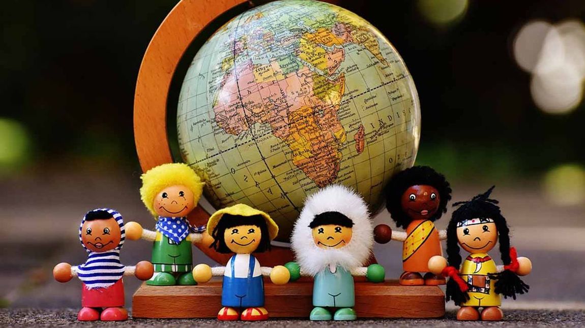 Kinder aus verschiedenen Nationen als Puppen vor einem Globus.